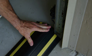 A hand applying a garage door flood barrier to the garage floor